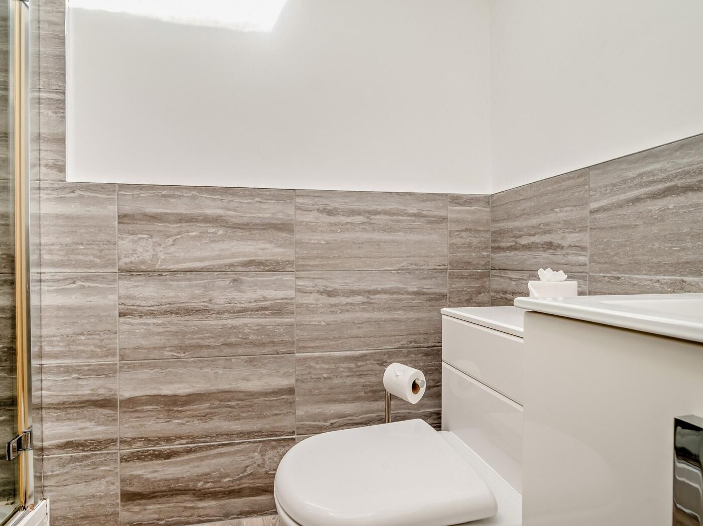 A modern bathroom with a toilet, a towel dispenser, and a glass shower enclosure.