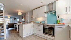 A modern kitchen with white cabinetry, a built-in oven, and a teal backsplash. - 2 Bed in Newquay (oc-75578) (Newquay)