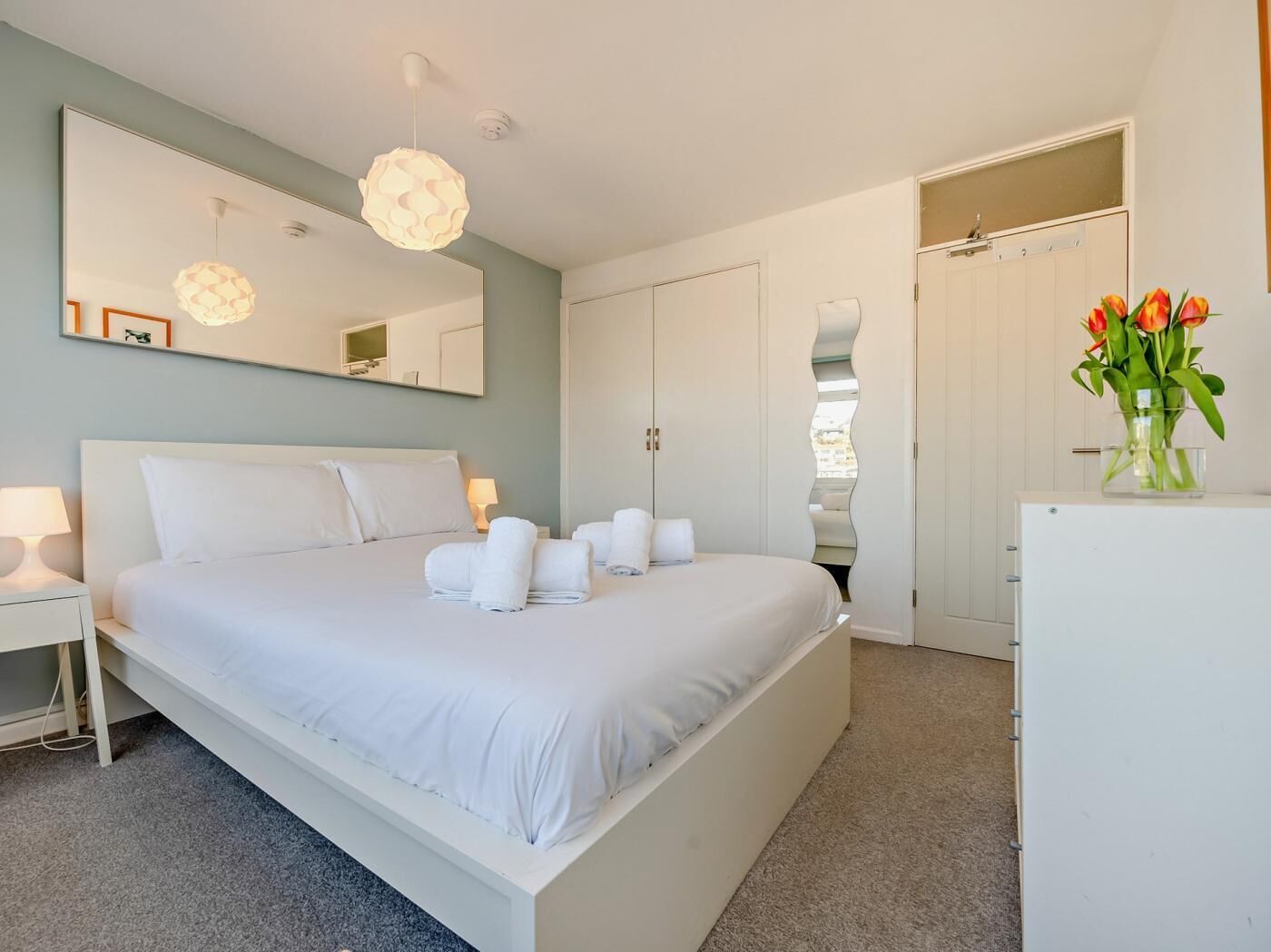 Une chambre d’hôtel moderne équipée d’un grand lit, d’un miroir, d’une armoire et d’un petit réfrigérateur.