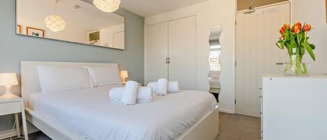 Une chambre d’hôtel moderne équipée d’un grand lit, d’un miroir, d’une armoire et d’un petit réfrigérateur.