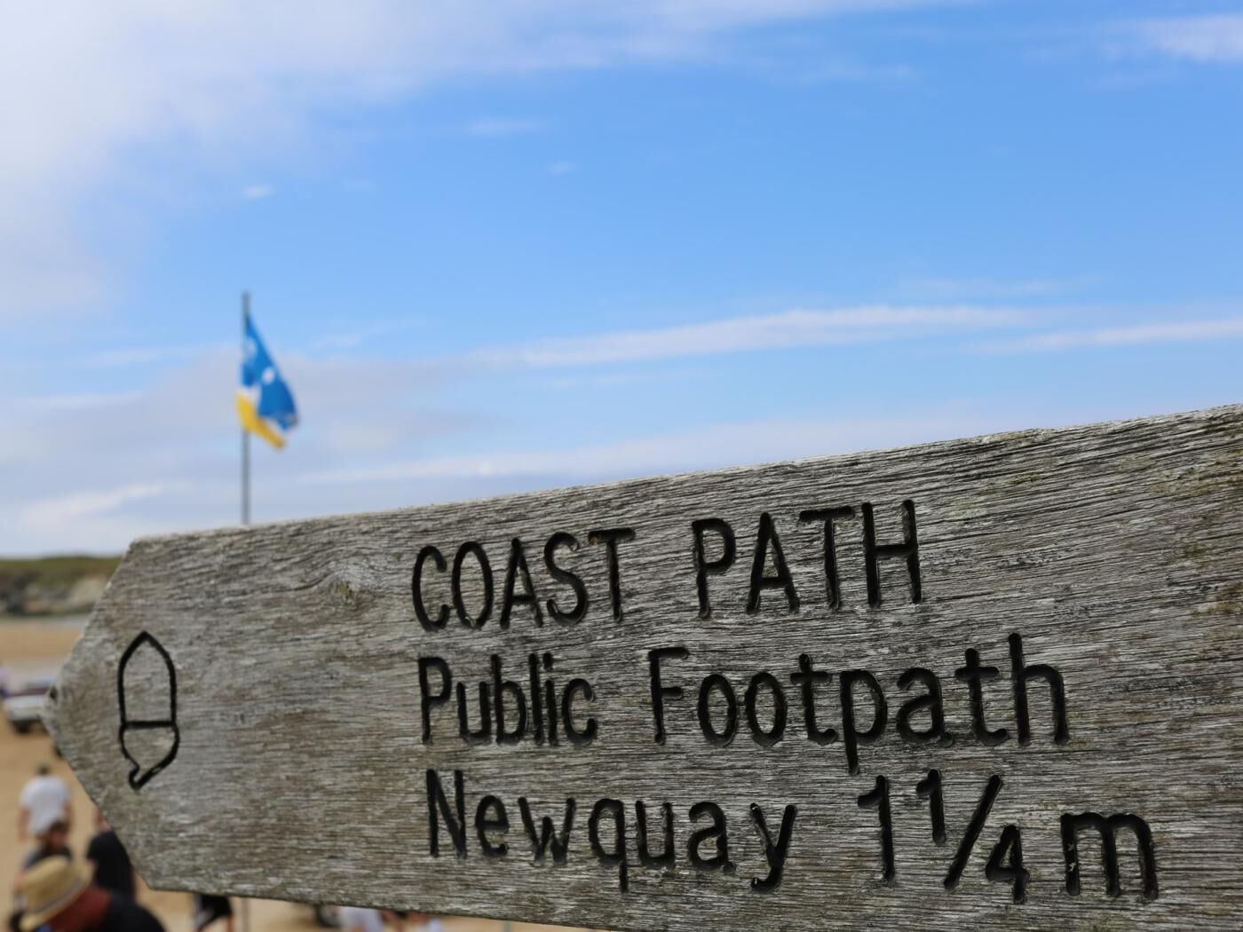 A wooden sign indicating a public footpath leading to Newquay, 1 1/4 miles away.