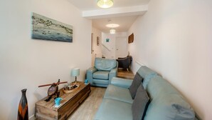 Uma sala de estar com sofá, mesa de centro, um quadro e escada que leva a outro cômodo.