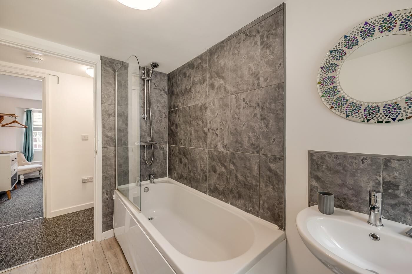 Une salle de bain moderne dotée d’une baignoire, d’une douche et d’un lavabo, avec des carreaux gris et un miroir décoratif.