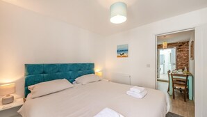 Quarto com uma cama grande, mesa de cabeceira, abajur, quadro e um espaço de refeições com mesa e cadeiras.