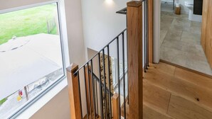 Ein modernes Interieur mit einer Holztreppe, Blick auf einen Garten durch ein großes Fenster und ein Badezimmer mit Toilette und Waschbecken.