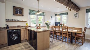 A kitchen with a central island, wooden cabinets, a washing machine, and a dining area with a bench and chairs. - 4 Bed in Worcester (oc-75601) (Halmond's Frome)
