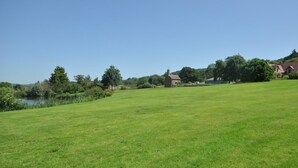 A grassy field with a pond, trees, and buildings in the distance. - 4 Bed in Worcester (oc-75601) (Halmond's Frome)