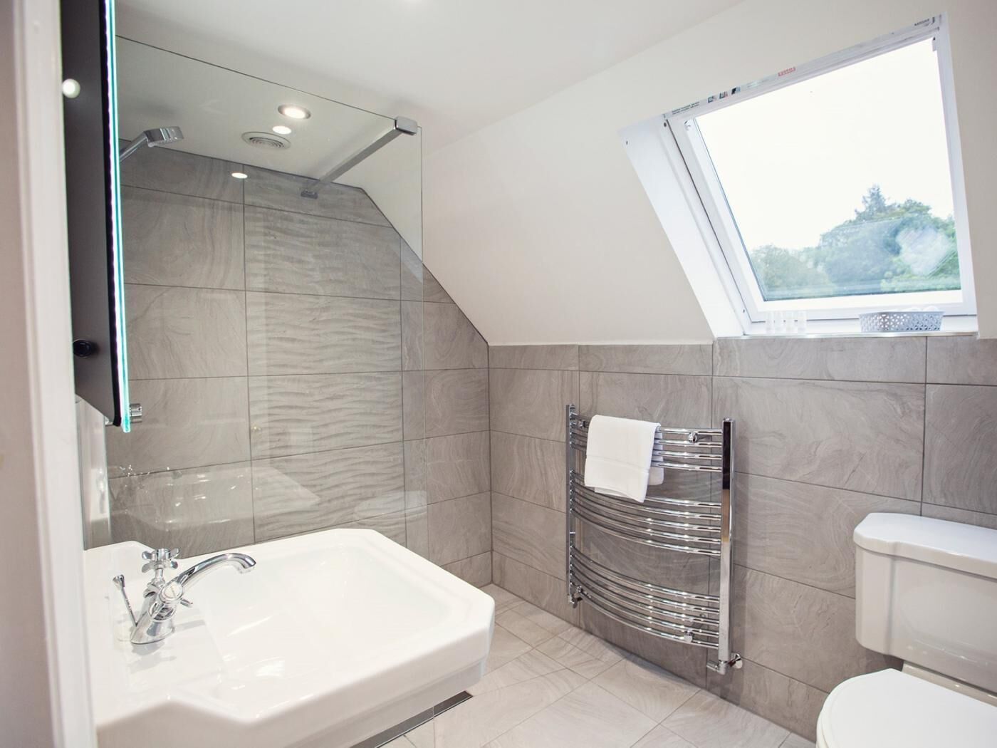 Ein modernes Badezimmer mit einer großen Badewanne, einer Duschkabine aus Glas, einem Handtuchhalter und einem Fenster für natürliches Licht.