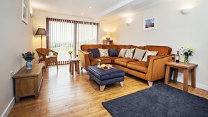 A modern living room with a sectional sofa, a small table, a chair, and a large window with blinds. - 4 Bed in Worcester (oc-75601) (Halmond's Frome)