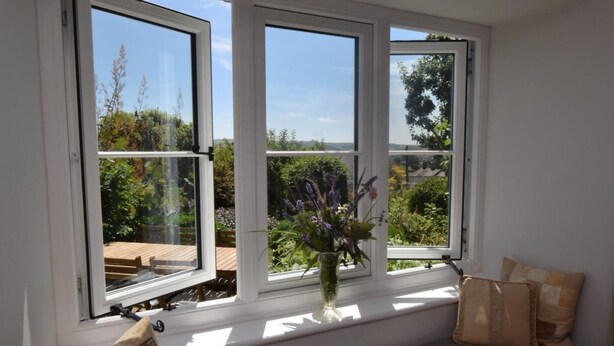 Una habitación con un asiento junto a la ventana, un jarrón con flores y vistas al verdor.