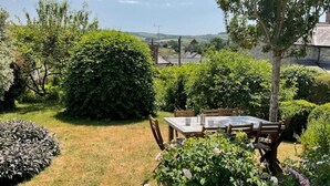 Un jardín con una mesa y sillas, rodeado de plantas y vistas al campo.