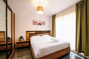 A hotel room with a bed, a bedside table, a nightstand, a mirror, a painting, a window with curtains, and a ceiling light fixture. - Gold 3 Apartment (Cannes)