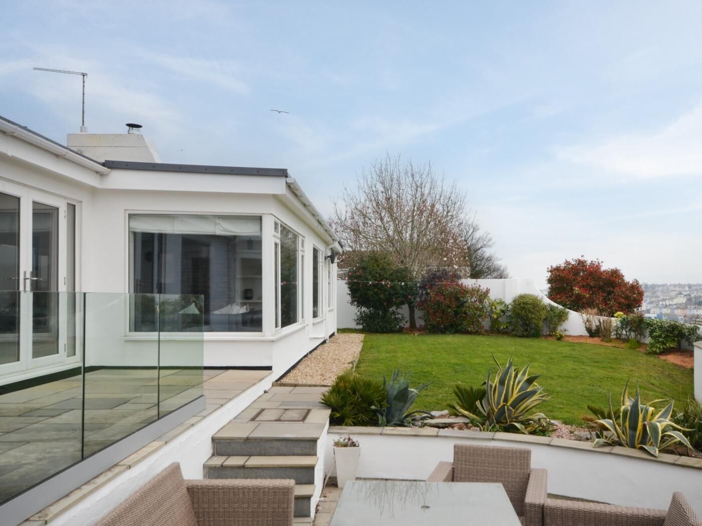 A modern house with a glass balcony, a well-maintained lawn, and outdoor seating.