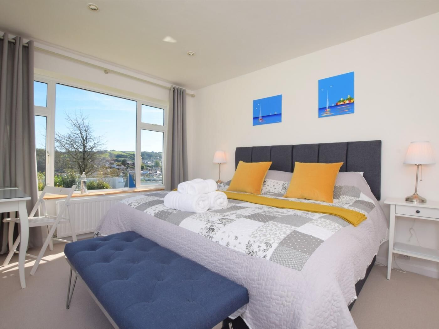 Ein Schlafzimmer mit einem großen Bett, zwei Nachttischen, einer Bank und Blick ins Freie.