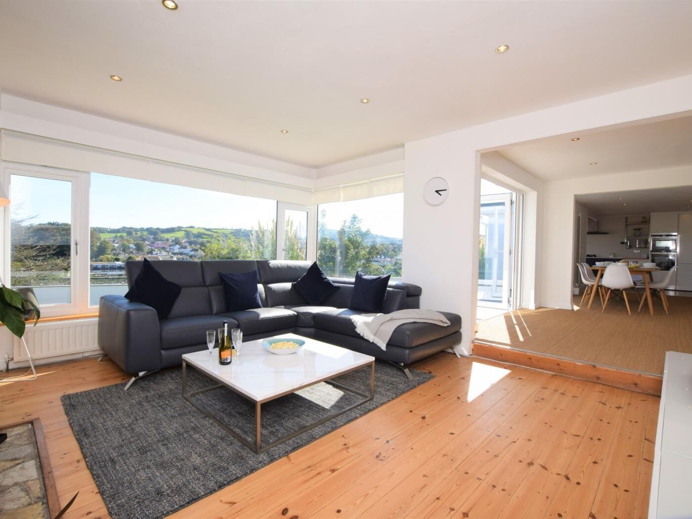 A modern living room with a sectional sofa, a coffee table, and large windows offering a view of the outdoors.