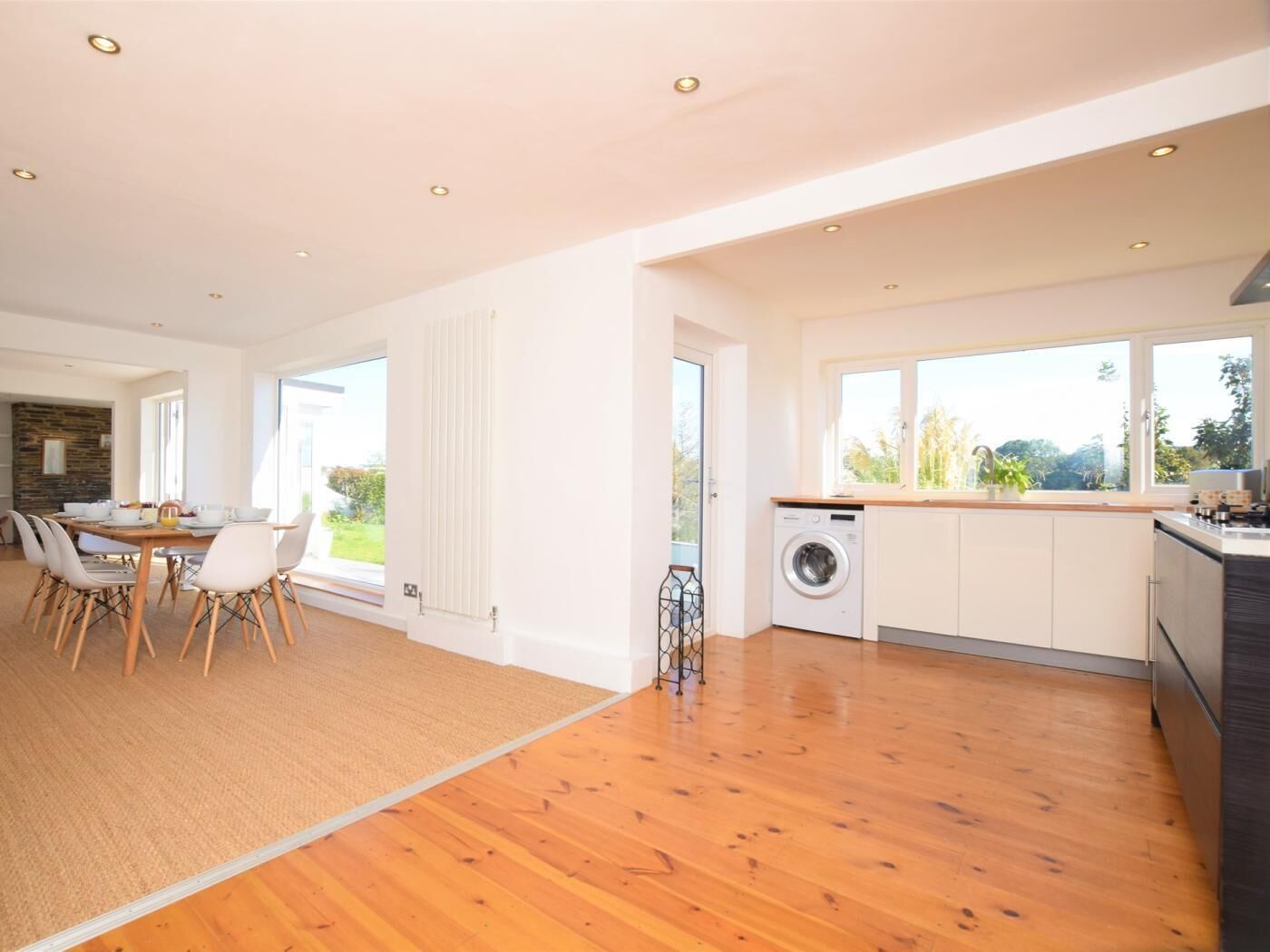 A modern kitchen with a washing machine, wooden flooring, and large windows.