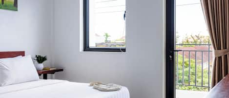 A hotel room with a bed, a window, a door, a small table with a plant, and a view of the outside.