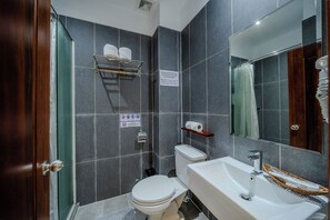 A bathroom with a toilet, sink, and shower area. There are signs on the wall, a towel rack, and a shelf with toiletries. - Onederz Kampot (Kampot)