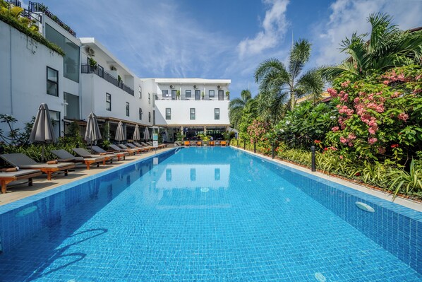 A swimming pool with lounge chairs and umbrellas, surrounded by greenery and a building with balconies. - Onederz Kampot (Kampot)