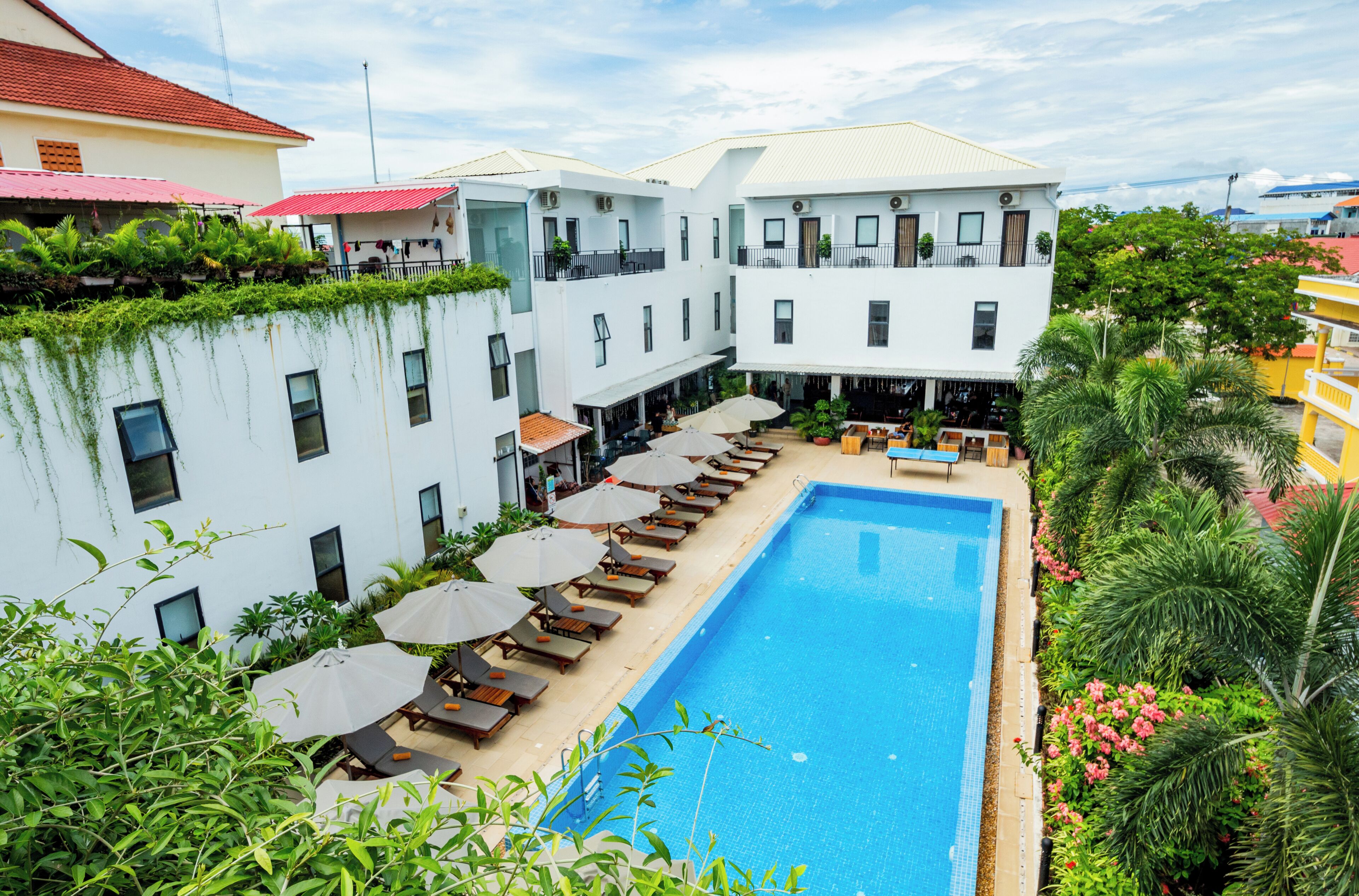 Un hotel con piscina, tumbonas y una zona de estar exterior cubierta.