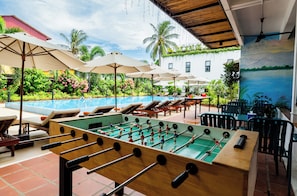 A pool area with lounge chairs, umbrellas, and a foosball table.