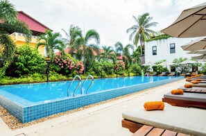 A swimming pool with lounge chairs and umbrellas, surrounded by tropical plants and buildings. - Onederz Kampot (Kampot)