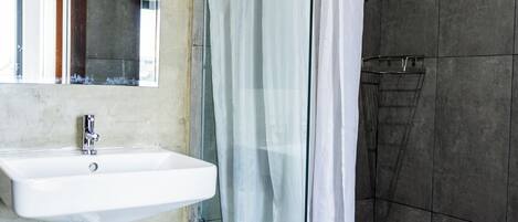 Een badkamer met een witte wastafel, een douchecabine van glas en een spiegel.