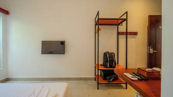 Een hotelkamer met een bed, een bureau met stoel, een plank met tas, een kapstok en een deur.