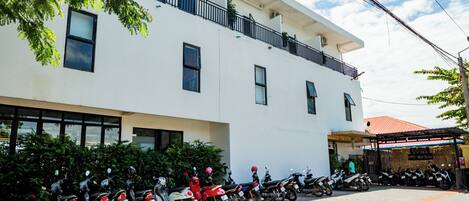Un edificio blanco con varias ventanas y una fila de motocicletas estacionadas adelante.