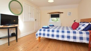Une chambre à coucher avec un lit, un téléviseur posé sur un meuble, une fenêtre et une porte.