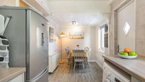 Een kleine keuken met een koelkast, wasmachine, eettafel en stoelen.