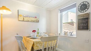 Een eetgedeelte met een gedekte tafel voor twee personen, een schilderij aan de muur, een klok en een raam met uitzicht.