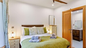 Quarto com cama, mesas de cabeceira, um criado-mudo, uma porta de madeira e um banheiro visível pela porta.