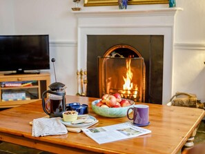 Ein gemütliches Zimmer mit Kamin, einer Kaffeemaschine, einer Obstschale und einem Fernseher.