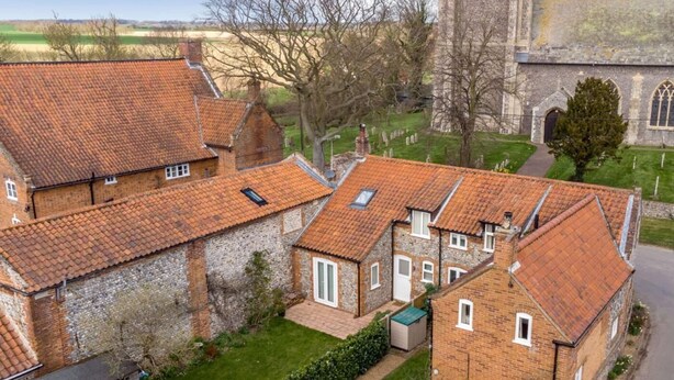 Un ensemble de maisons traditionnelles en briques, avec des toits couverts de tuiles rouges, une église en pierre et un ciel dégagé.