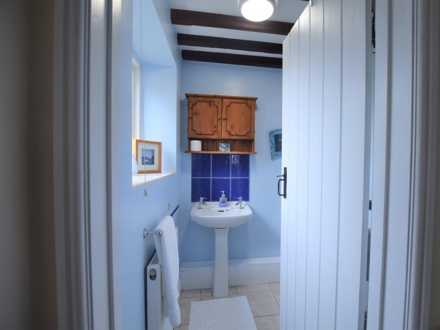 A bathroom with a pedestal sink, wooden cabinets, a framed picture on the wall, and a white towel hanging on a rack.