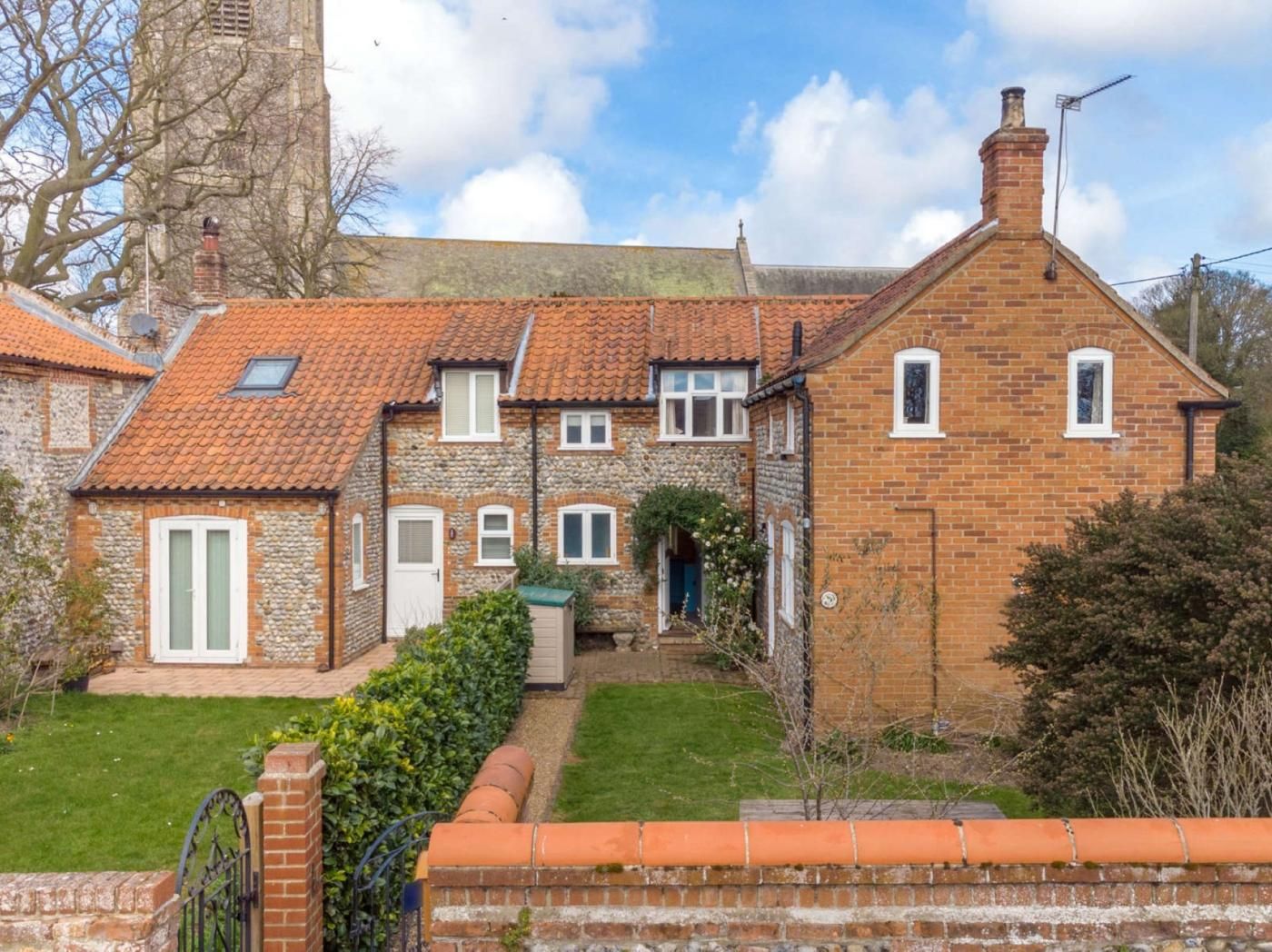 A traditional brick house with a tiled roof, a small garden, and a stone wall.