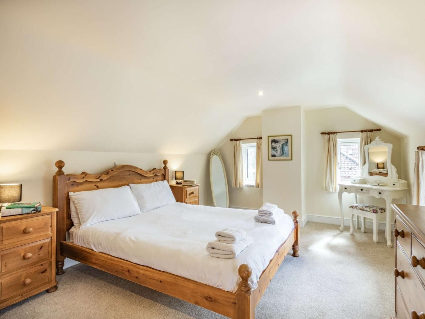 A bedroom with a wooden bed, bedside tables, a dresser, a desk, and a mirror.