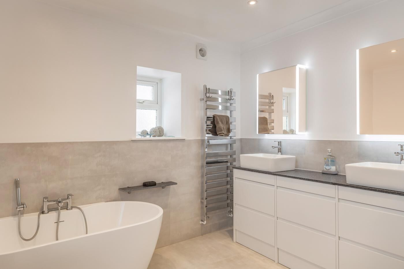 A modern bathroom with a freestanding bathtub, a vanity with a large mirror, and a towel rack.