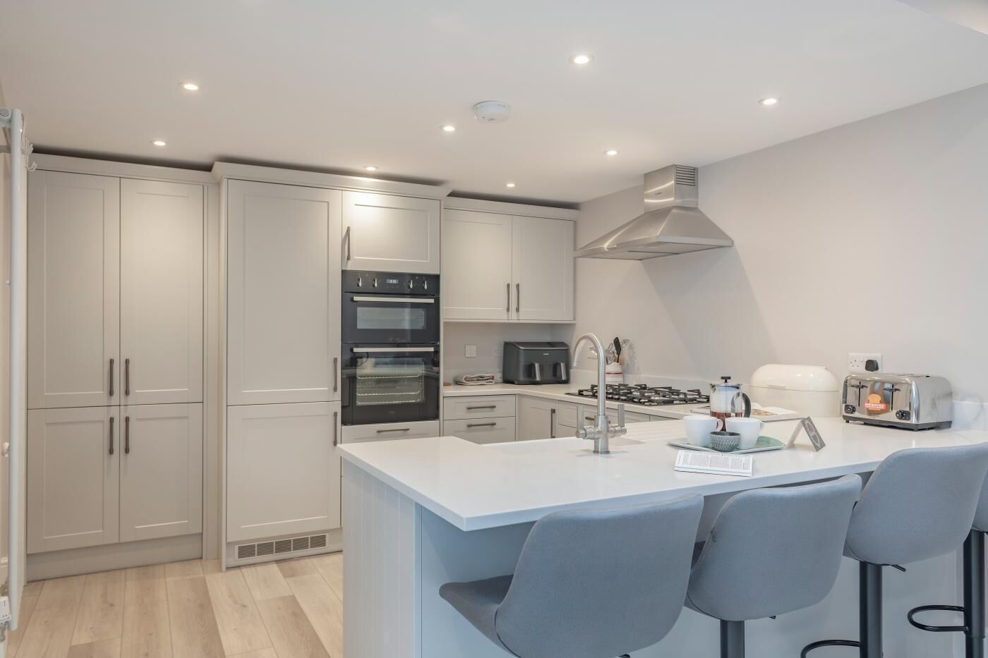 A modern kitchen with a central island, built-in ovens, a gas stove, and bar stools.