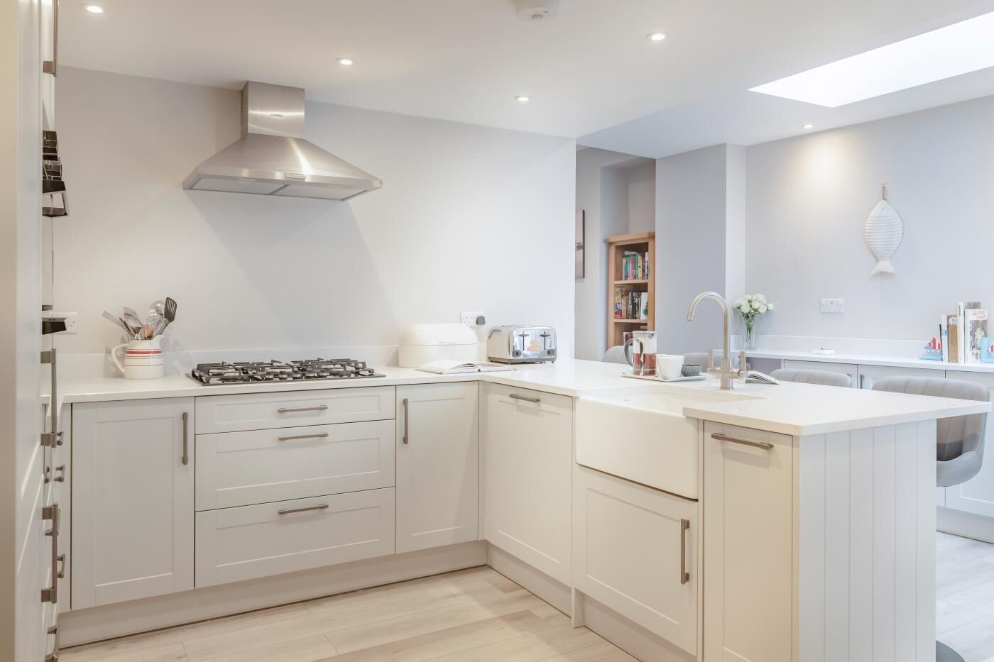A modern kitchen with white cabinetry, a stainless steel range hood, a built-in oven, and a countertop with a toaster.