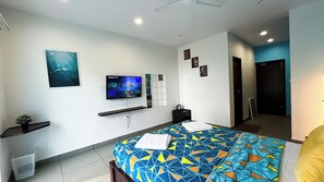 A modern hotel room with a bed, a flat-screen TV, a coffee maker, and a door leading to another room.