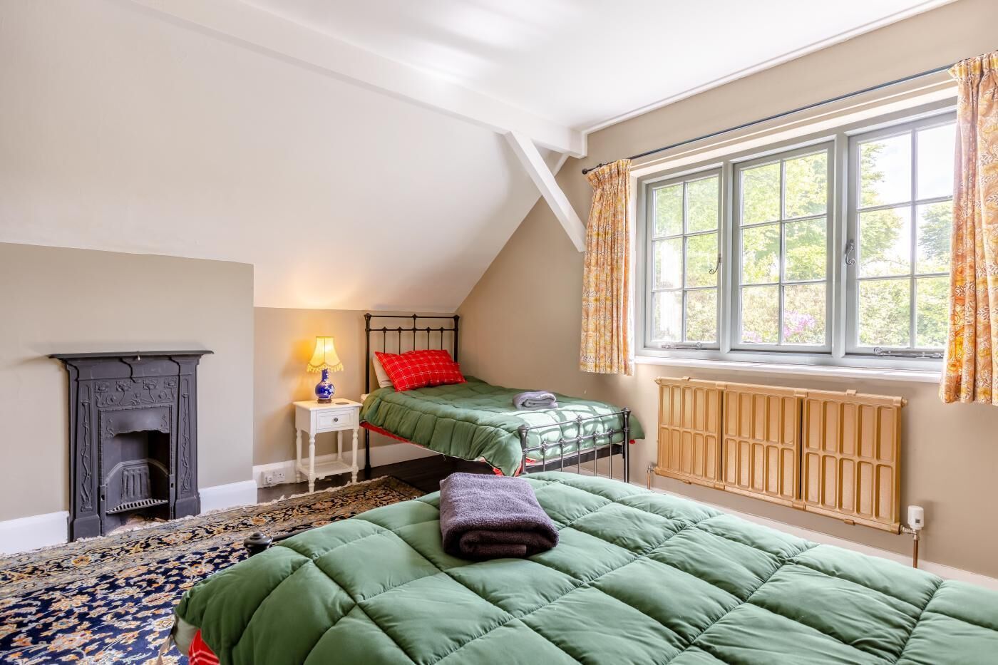 A room with two beds, a fireplace, a window with curtains, and a radiator.