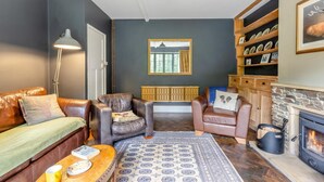 Een gezellige woonkamer met een open haard, leren banken, een kamerbreed tapijt en een boekenkast met decoratieve objecten.