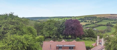 A rural house with a red roof, surrounded by greenery and fields.