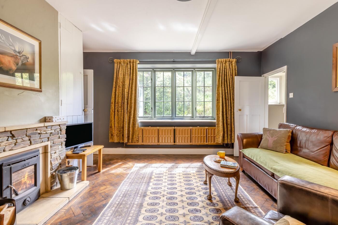 A living room with a stone fireplace, a television, a sofa, a coffee table, and a large window with curtains.