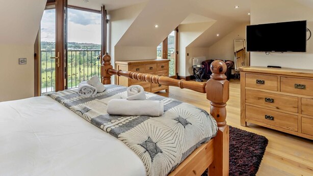 Ein Schlafzimmer mit Bett, Holzkommode, Fernseher und einem Balkon mit Blick.