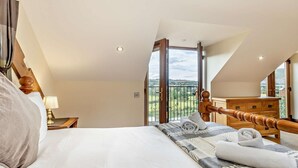 Ein Schlafzimmer mit einem großen Bett, einem hölzernen Kopfende, einem Nachttisch, einer Kommode und einem Balkon mit Blick.