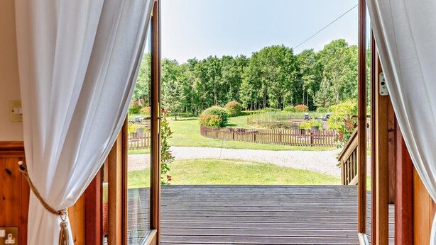 A view from a room with a wooden floor and a wooden railing, looking out to a grassy area with trees and a wooden fence.