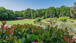 A garden with a wooden fence, a pond, and a building in the background.
